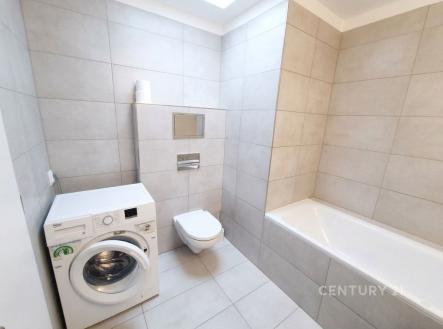 Koupelna s moderní dlažbou, vestavěnou vanou a pračkou. Světlé obklady zajišťují čistý vzhled a prostornost. | Pronájem bytu, 1+kk, 34 m²